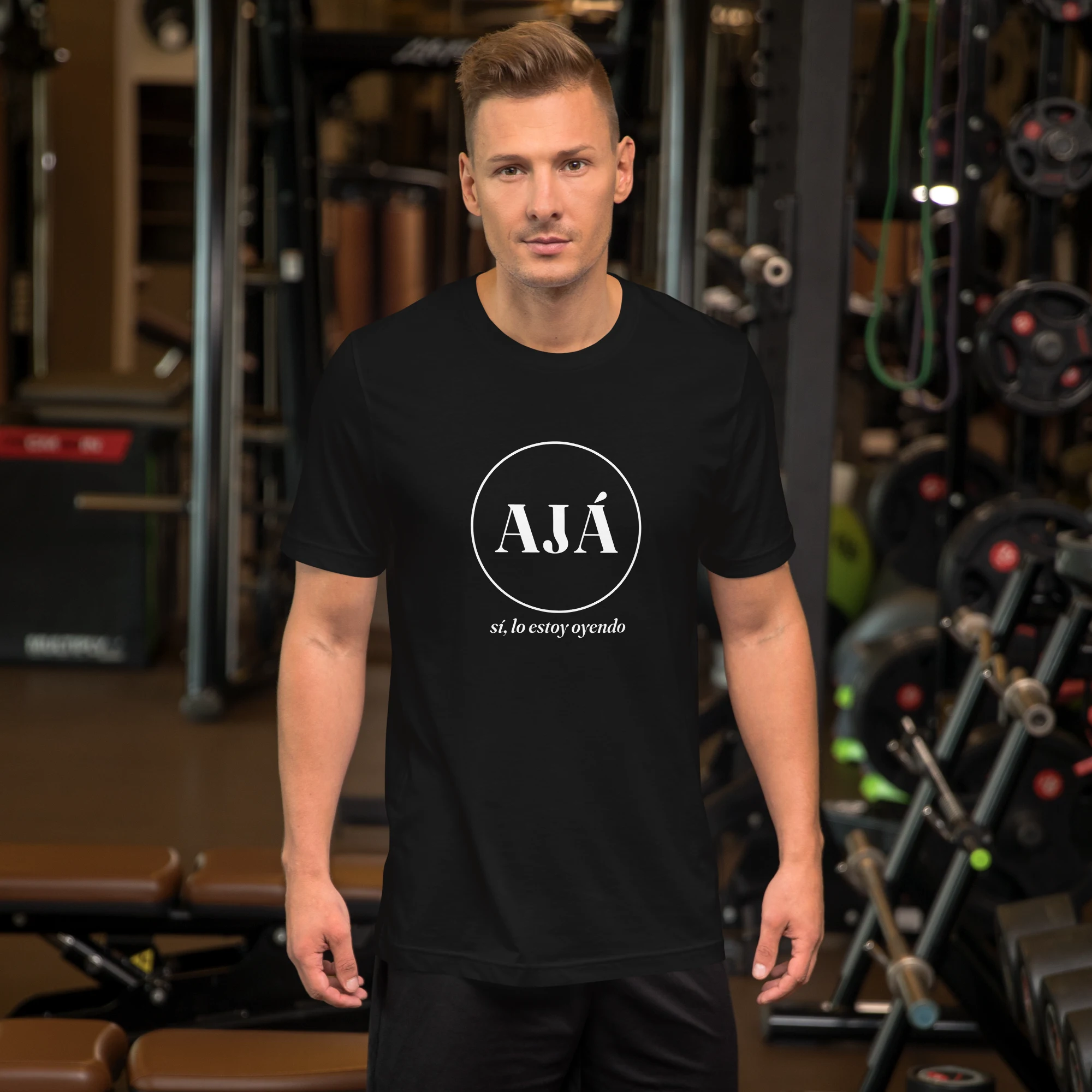 AJÁ badge tee on a man, black — white circle badge reading AJÁ with 'sí, lo estoy oyendo' tagline